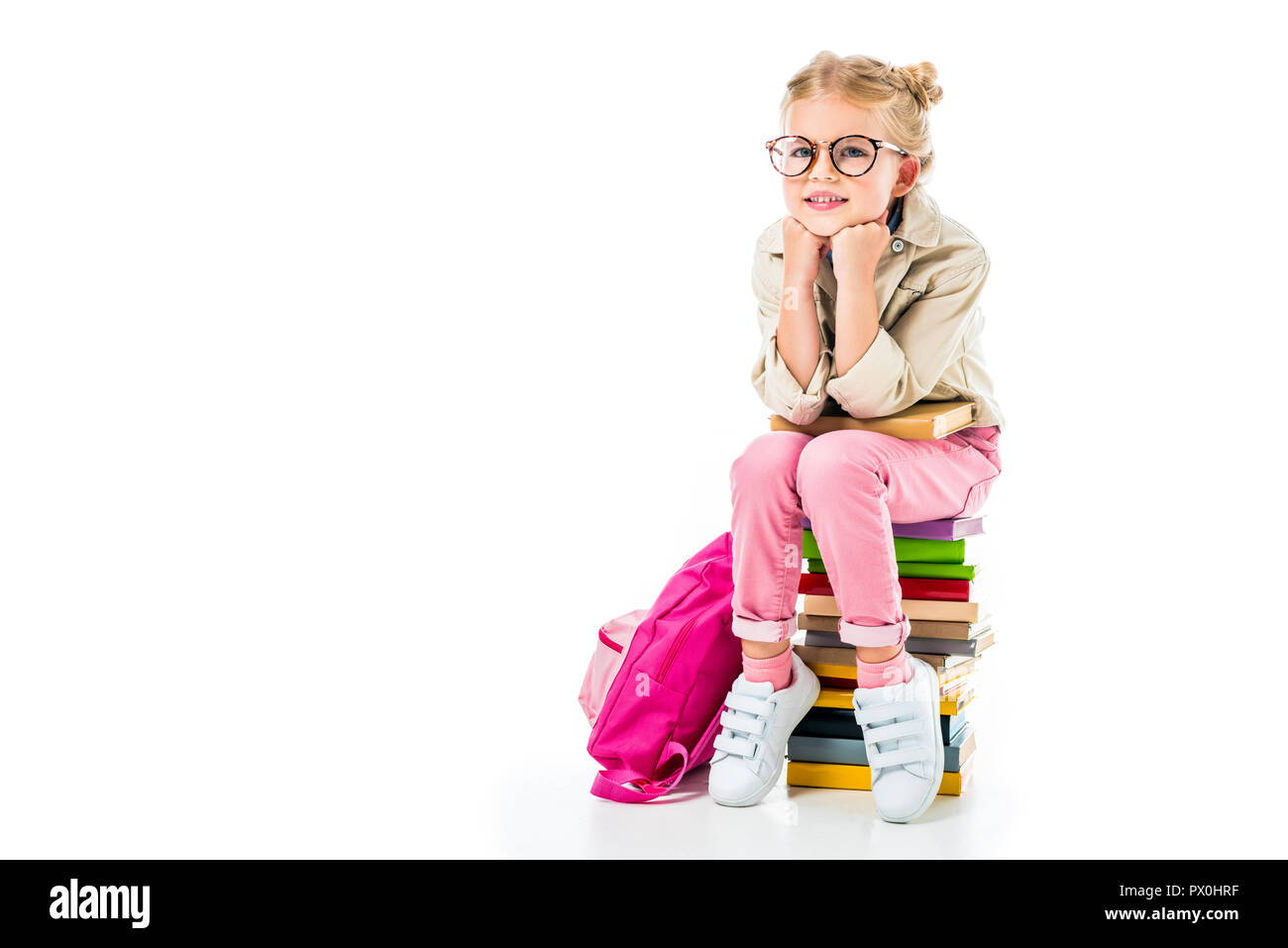 adorable smiling schoolgirl sitting on pile of books isolated on white ...