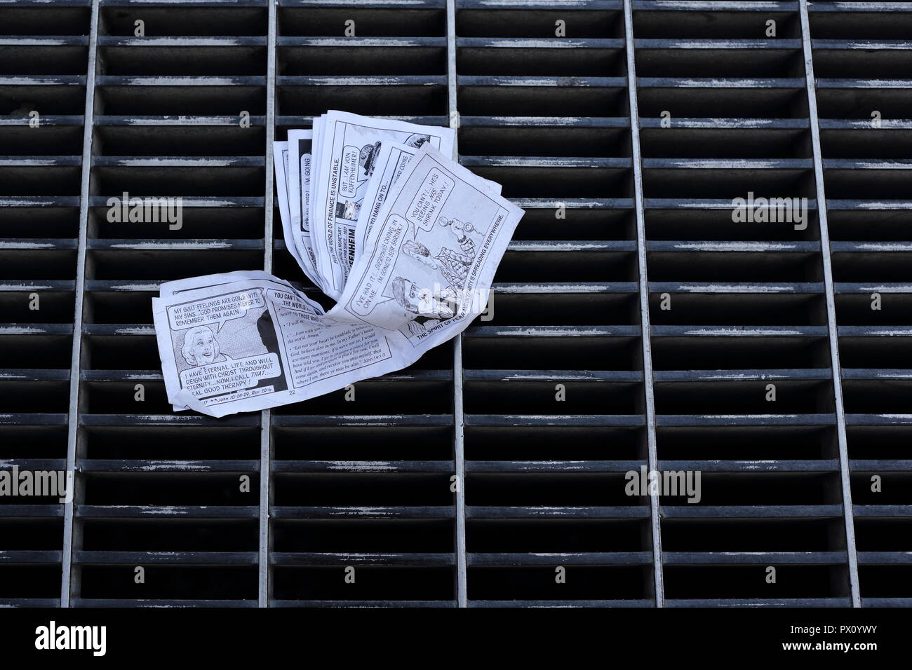 Crumpled up religious comic on street grate. Stock Photo