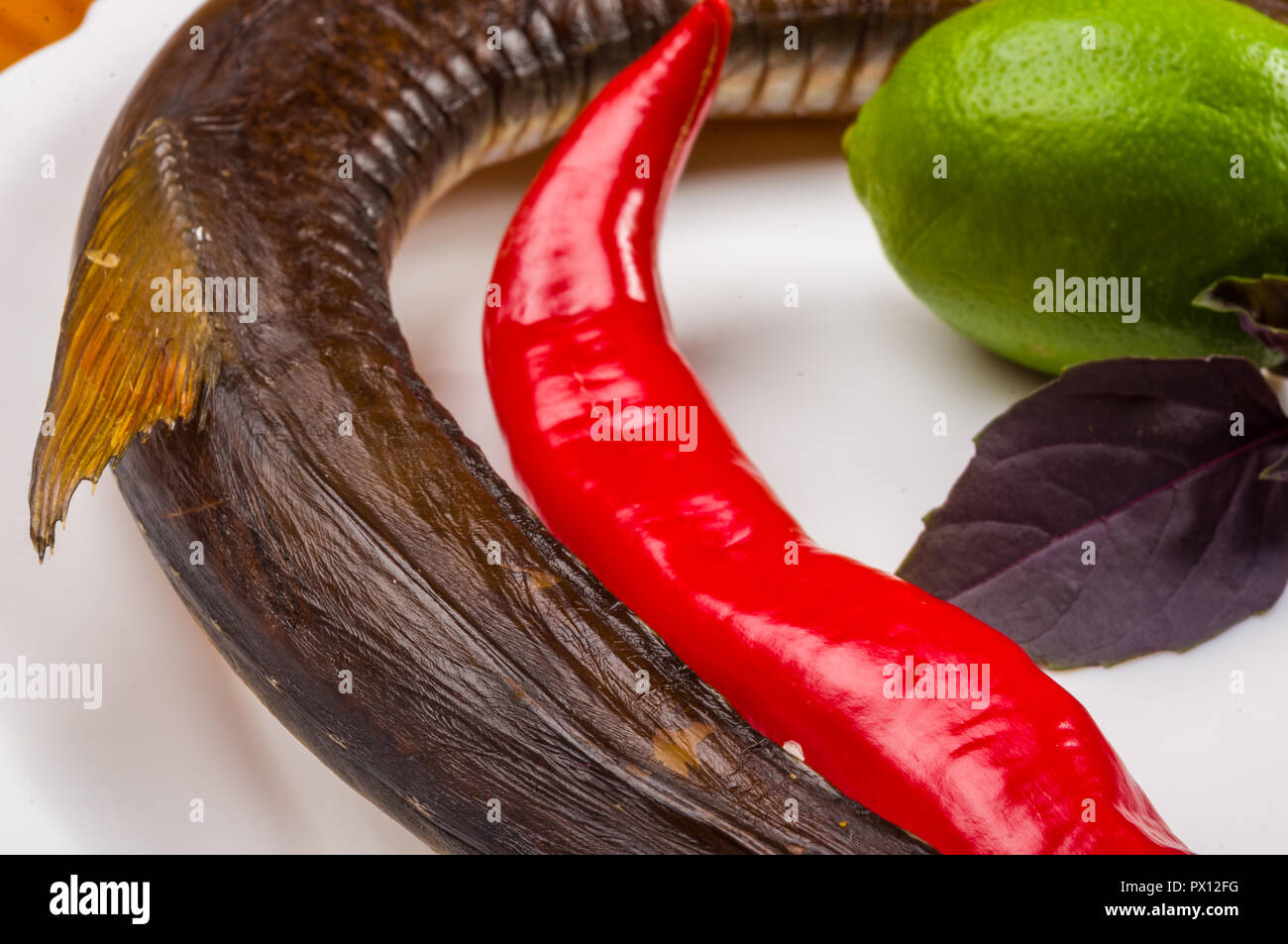 still life - smoked garfish with lime, Basil, green onions, chili, nori chips, spices, olive oil in a white ceramic dish, on a wooden table Stock Photo