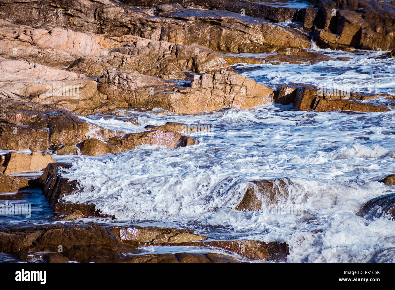 Closeup of a wave gently breaking over shallow rocks on the coast. Stock Photo
