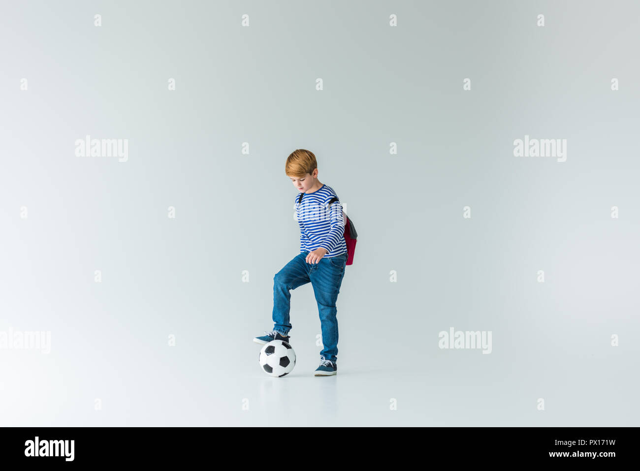 adorable schoolboy with backpack putting leg on fotball ball on white Stock Photo