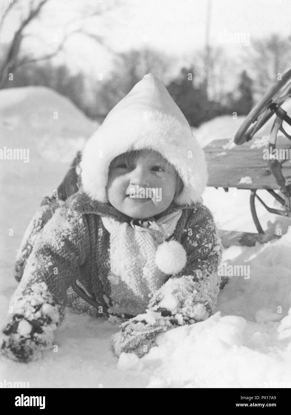 Winter in the 1940s. A child has fallen from the sledge but doesn't seem to mind. Sweden 1940s. Stock Photo