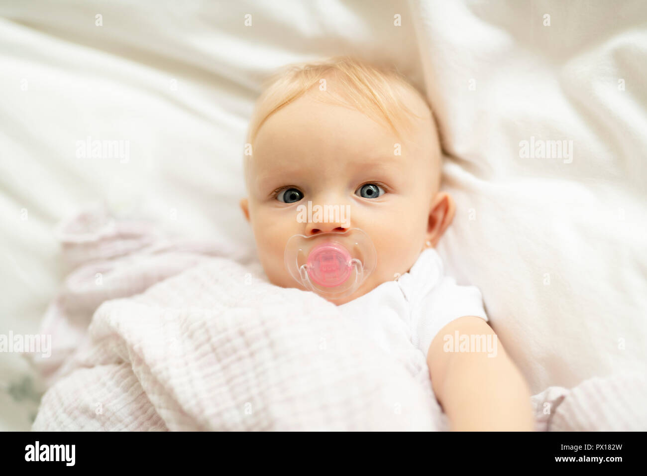 A cute baby with pacifier lying on a white bed Stock Photo Alamy