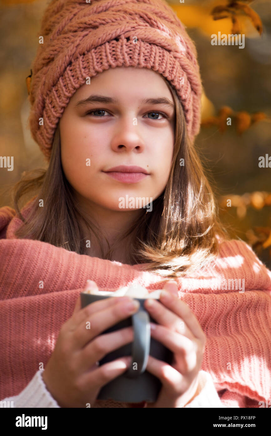 Portrait of pretty nice teenage girl drinking hot cocoa with marshmallows in autumn park Stock Photo