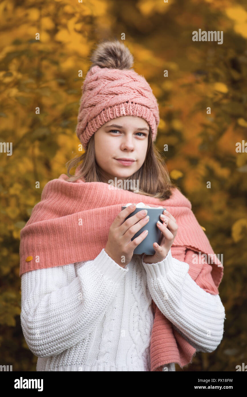 Portrait of pretty nice teenage girl drinking hot cocoa with marshmallows in autumn park Stock Photo