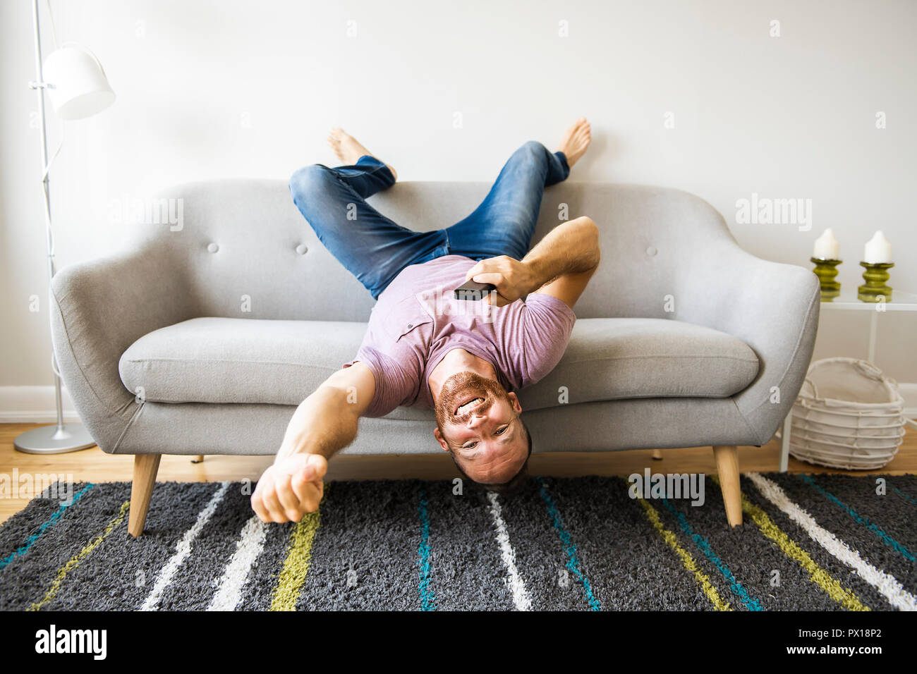Man listening tv upside down on the sofa with tv remote Stock Photo