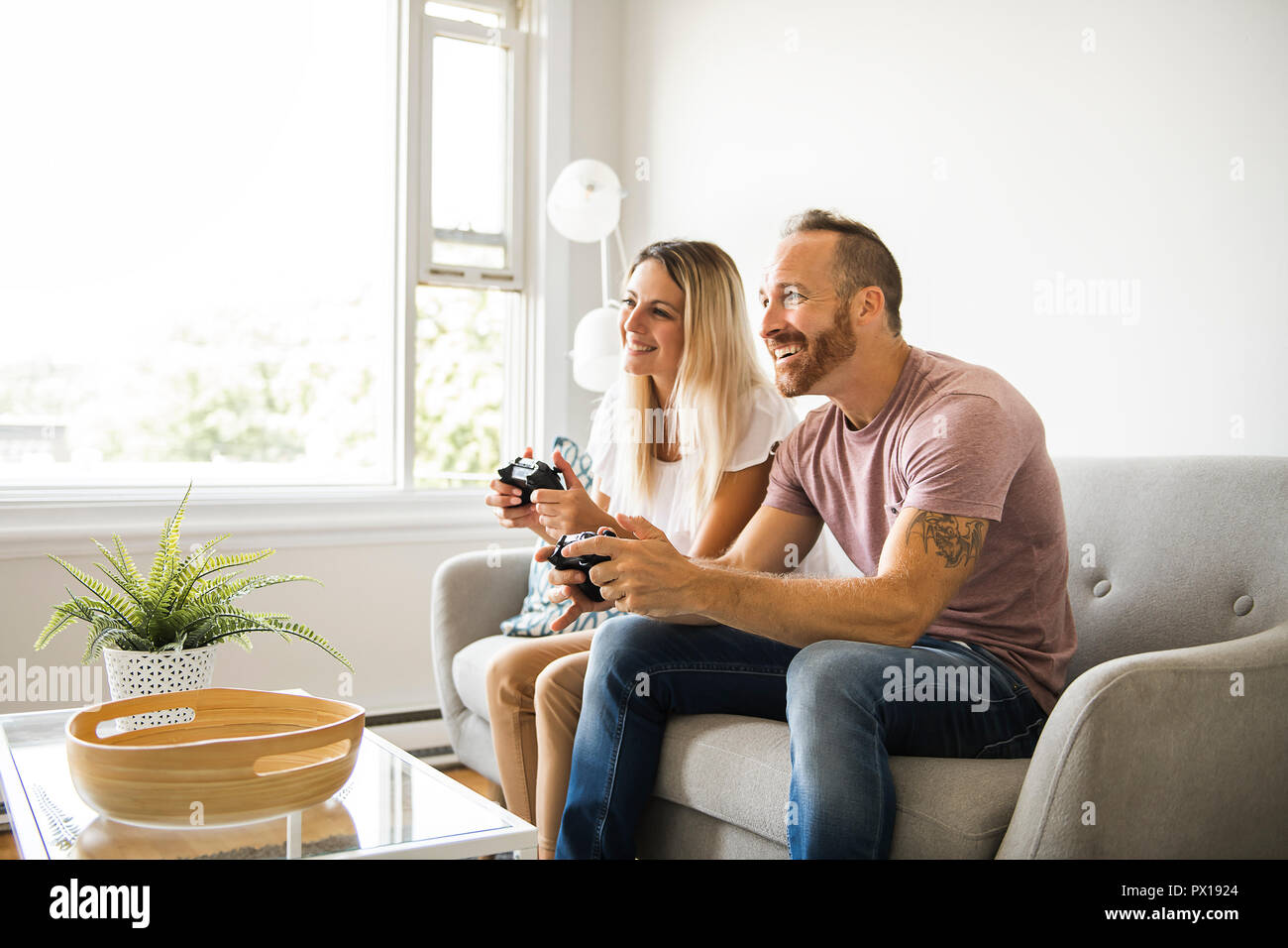 Couple playing video games at home, sitting on sofa Stock Photo Alamy
