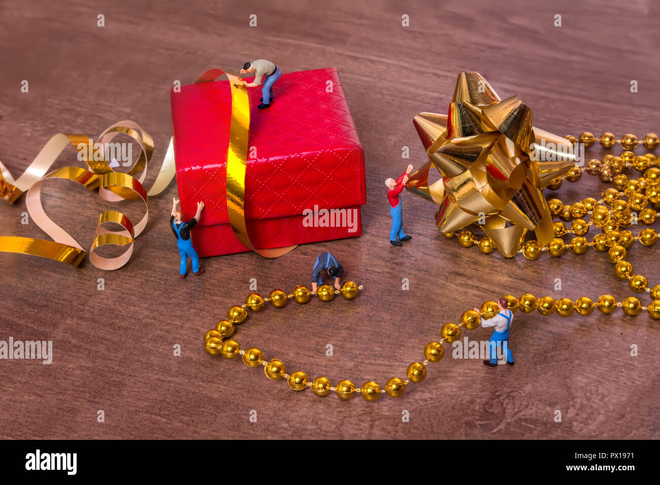 Creative concept with miniature people and a gift box on a wooden background. The process of packing gifts. Gold ribbon, bow, festive beads. Stock Photo
