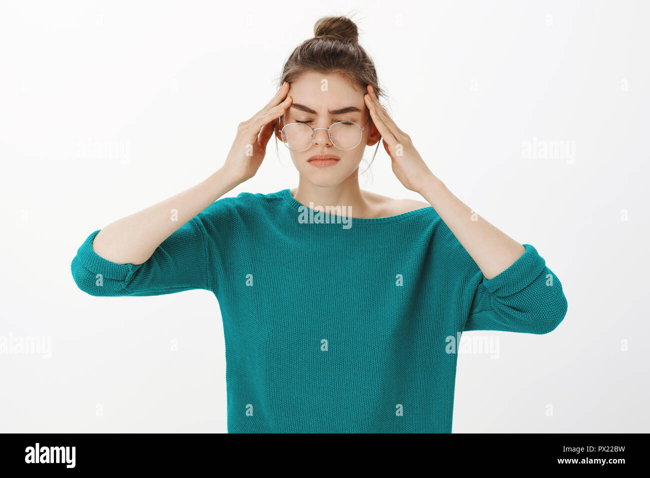 Just a sec, headache again. Portrait of intense gloomy and tired woman in casual outfit and glasses, closing eyes, touching temples and frowning while suffering migraine or painful feeling Stock Photo