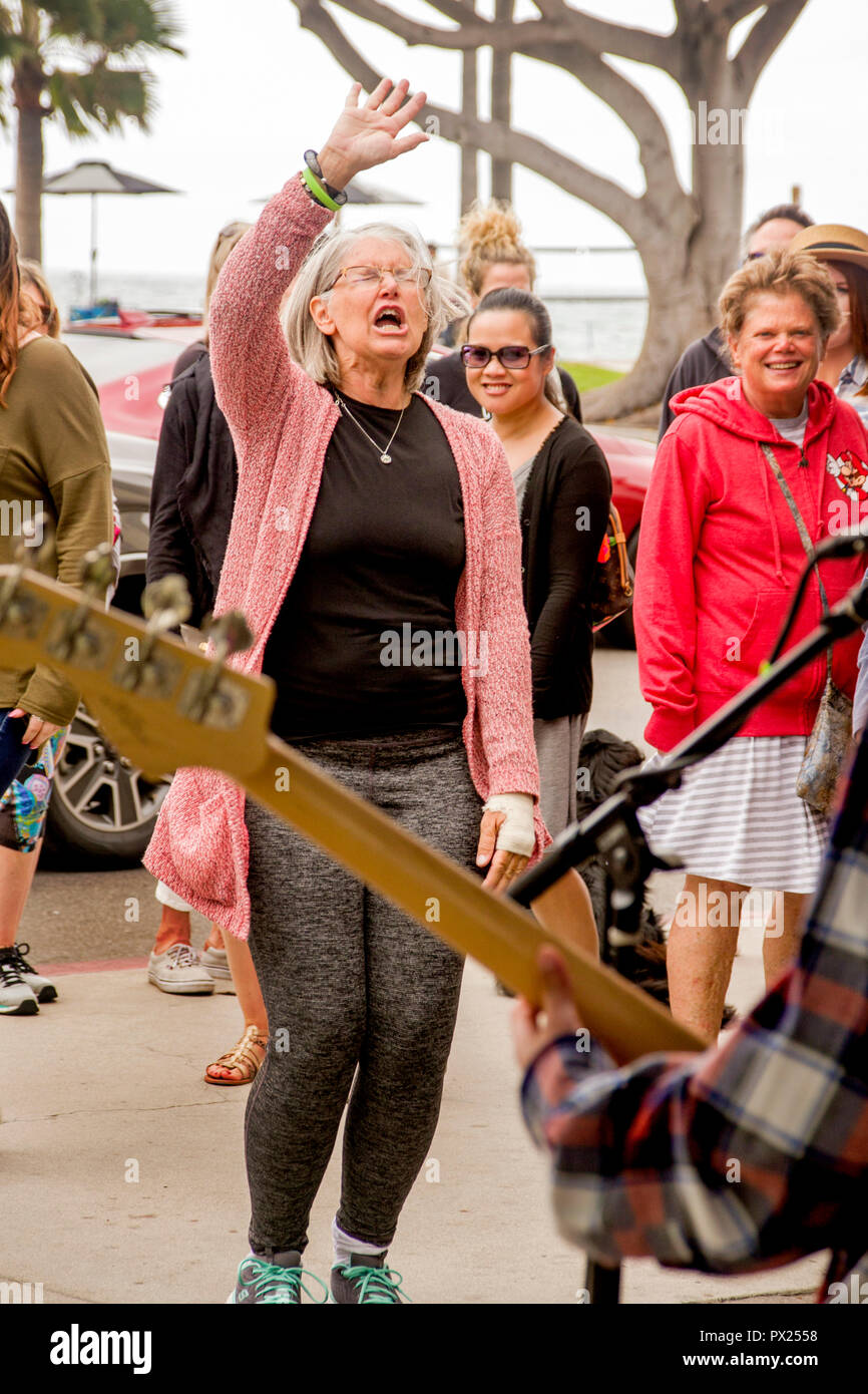 A senior woman reacts with enthusiastic enjoyment to a rock 'n roll band at an outdoor music festival in a Laguna Beach, CA, beachside park. Stock Photo