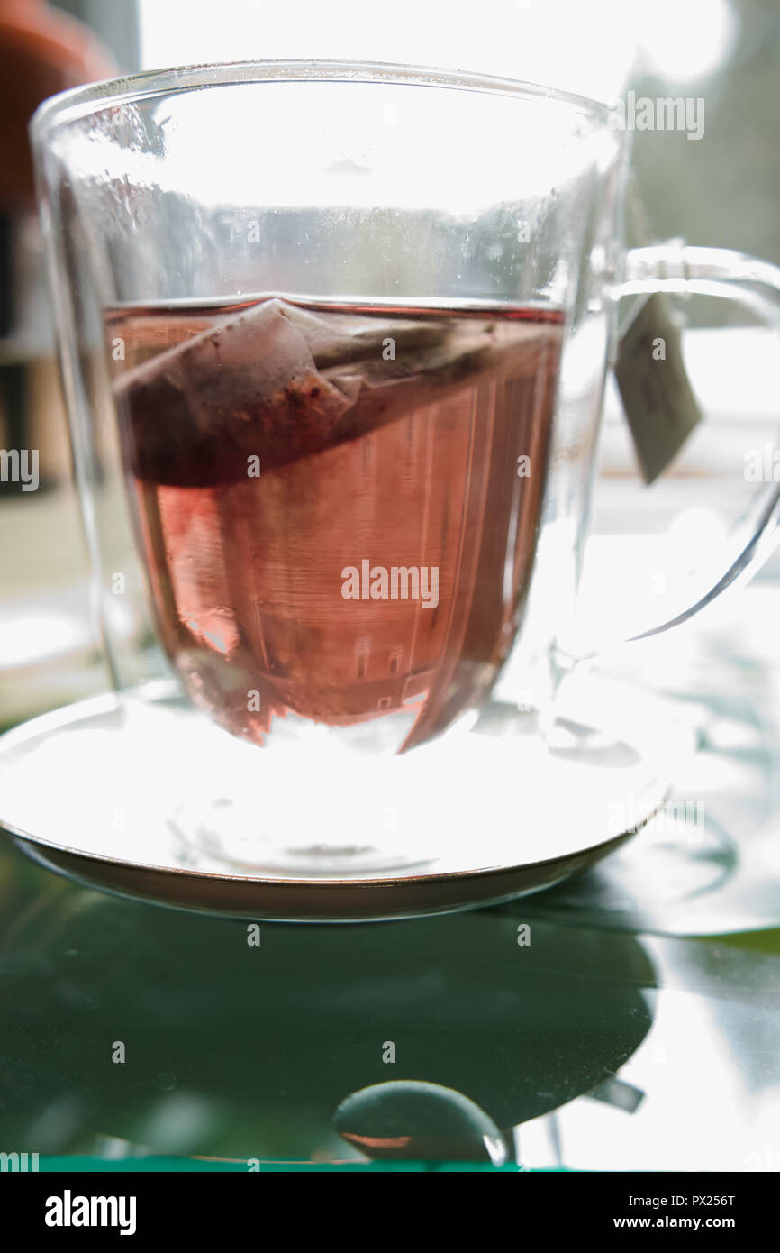 A black tea bag gives the glass cup a reddish colour. Stock Photo