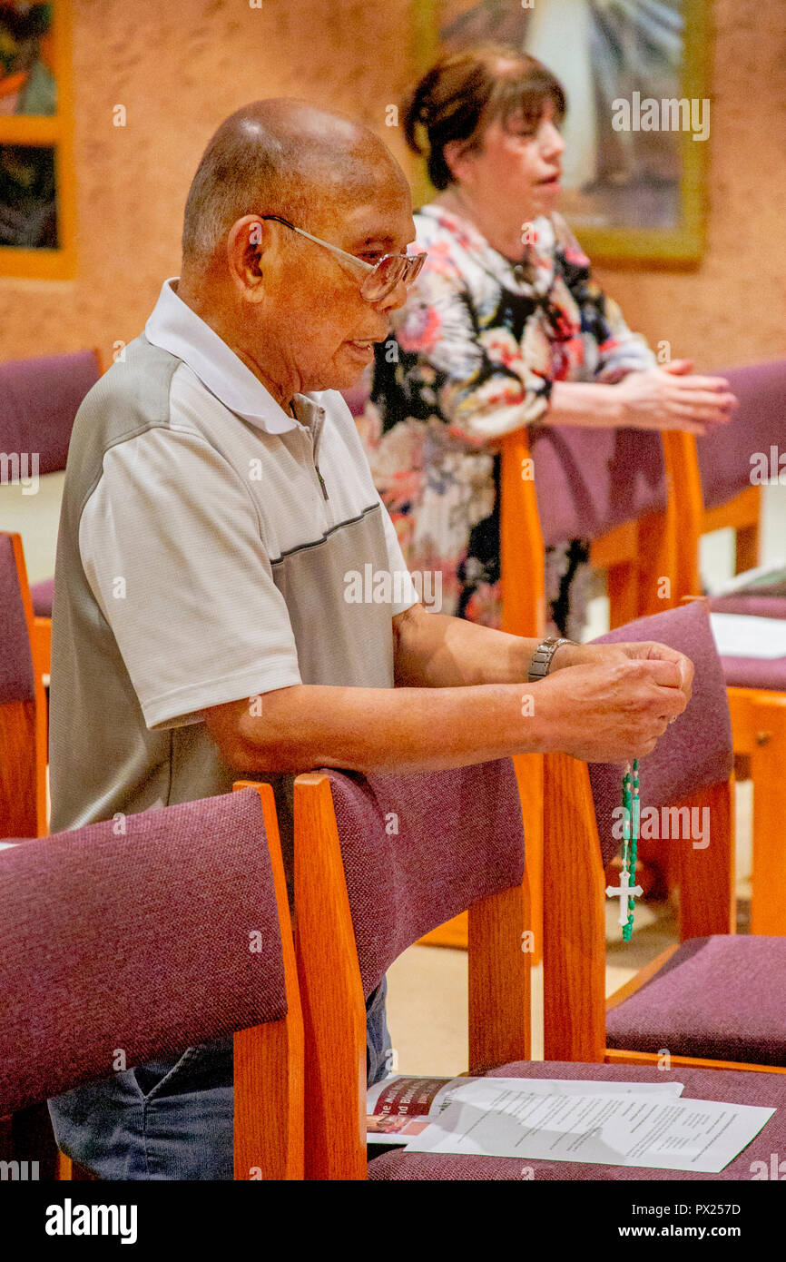 An elderly Vietnamese American man holds a rosary as he kneels in prayer during mass at a Laguna Niguel, CA, Catholic church. Stock Photo
