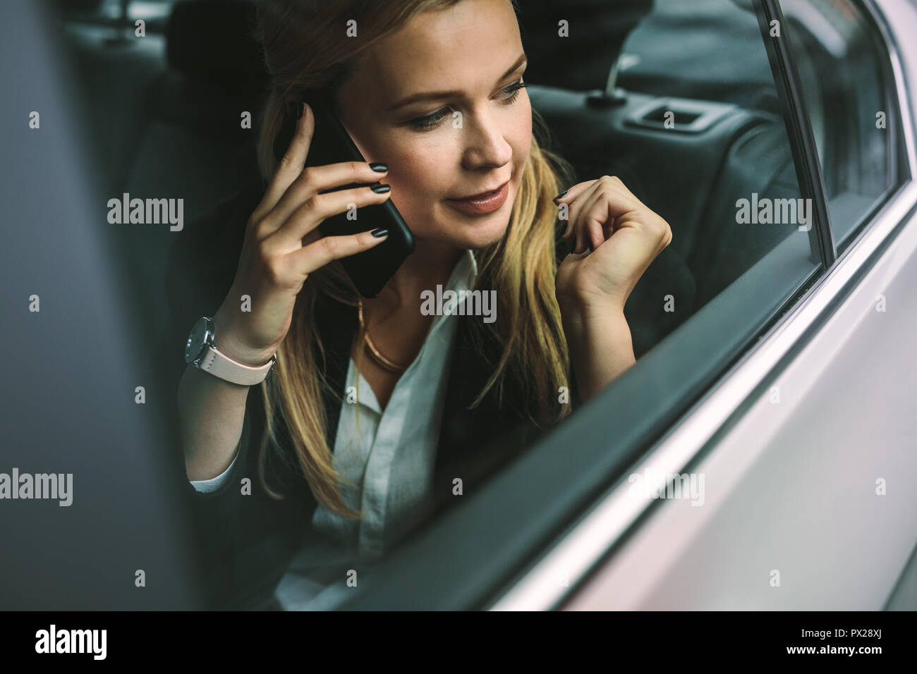 Young businesswoman talking on the cellphone while sitting on back seat of a car. Caucasian female executive travelling by a taxi and talking on mobil Stock Photo