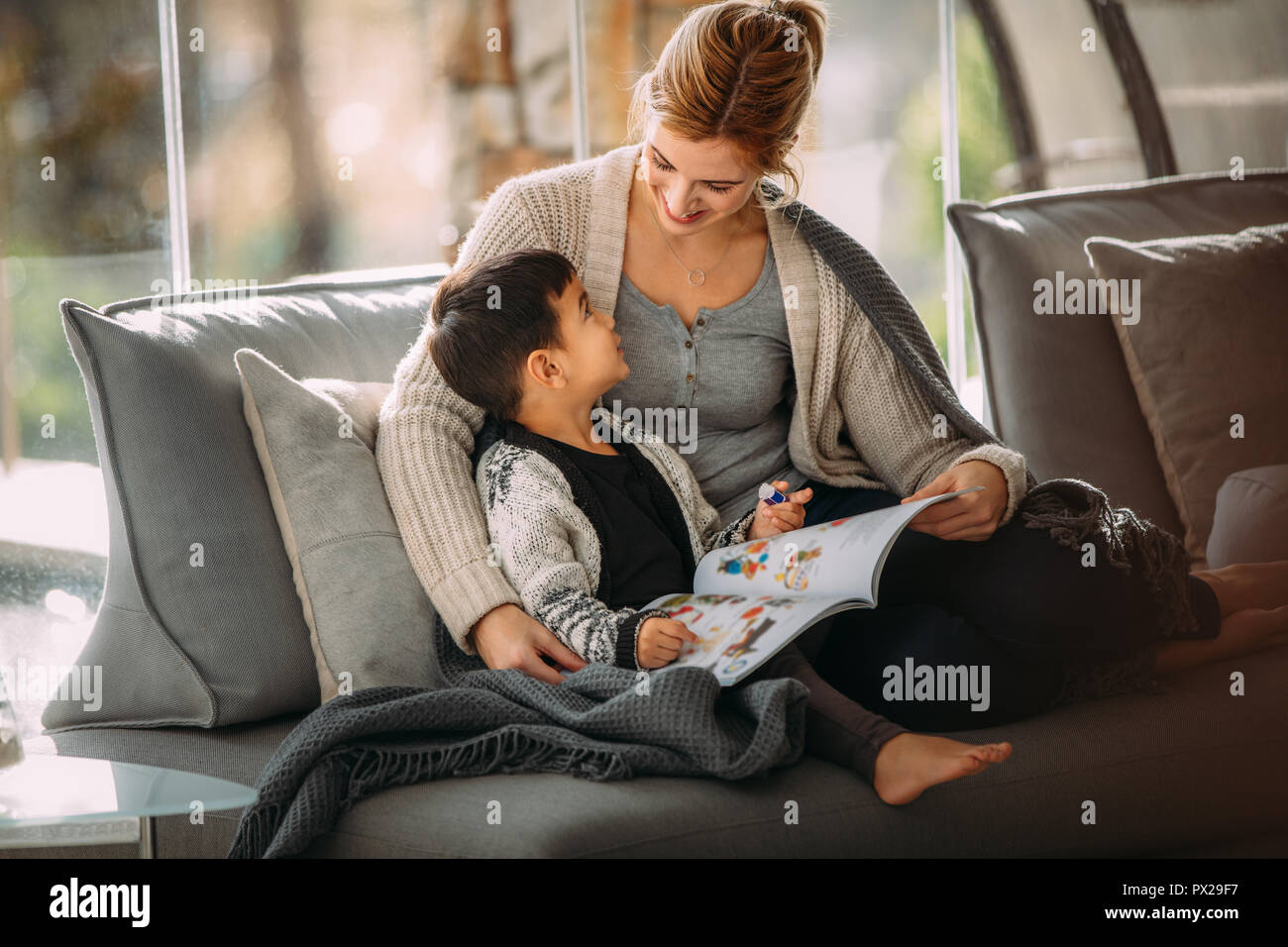 Happy mother and son sitting on couch with a story book living room. Woman and little boy with picture book at home. Stock Photo