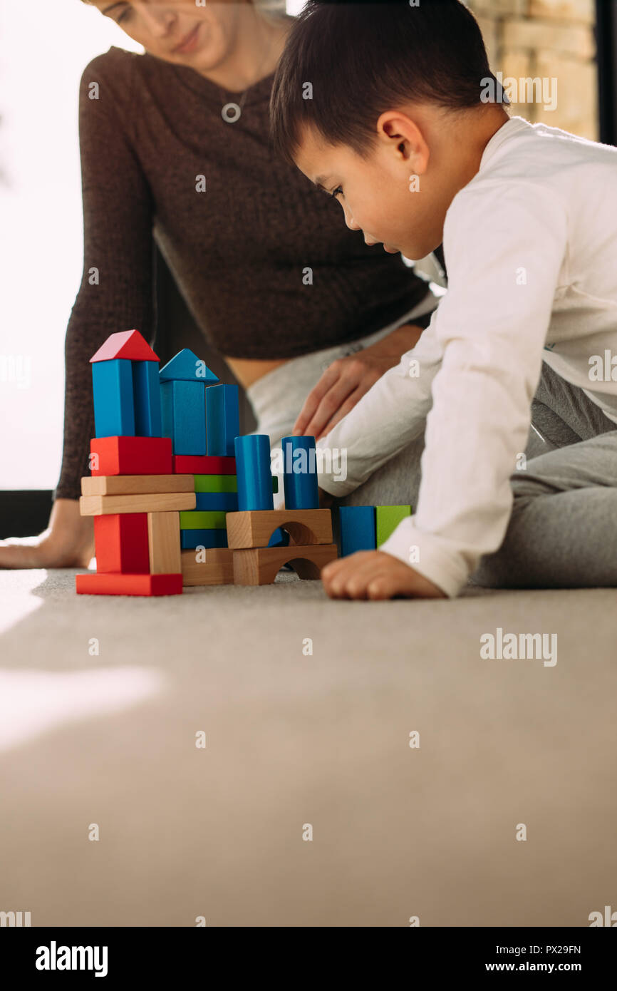 Cute child playing with colorful wooden blocks with his mother sitting by. Kid playing with colorful toys with mother at home. Stock Photo