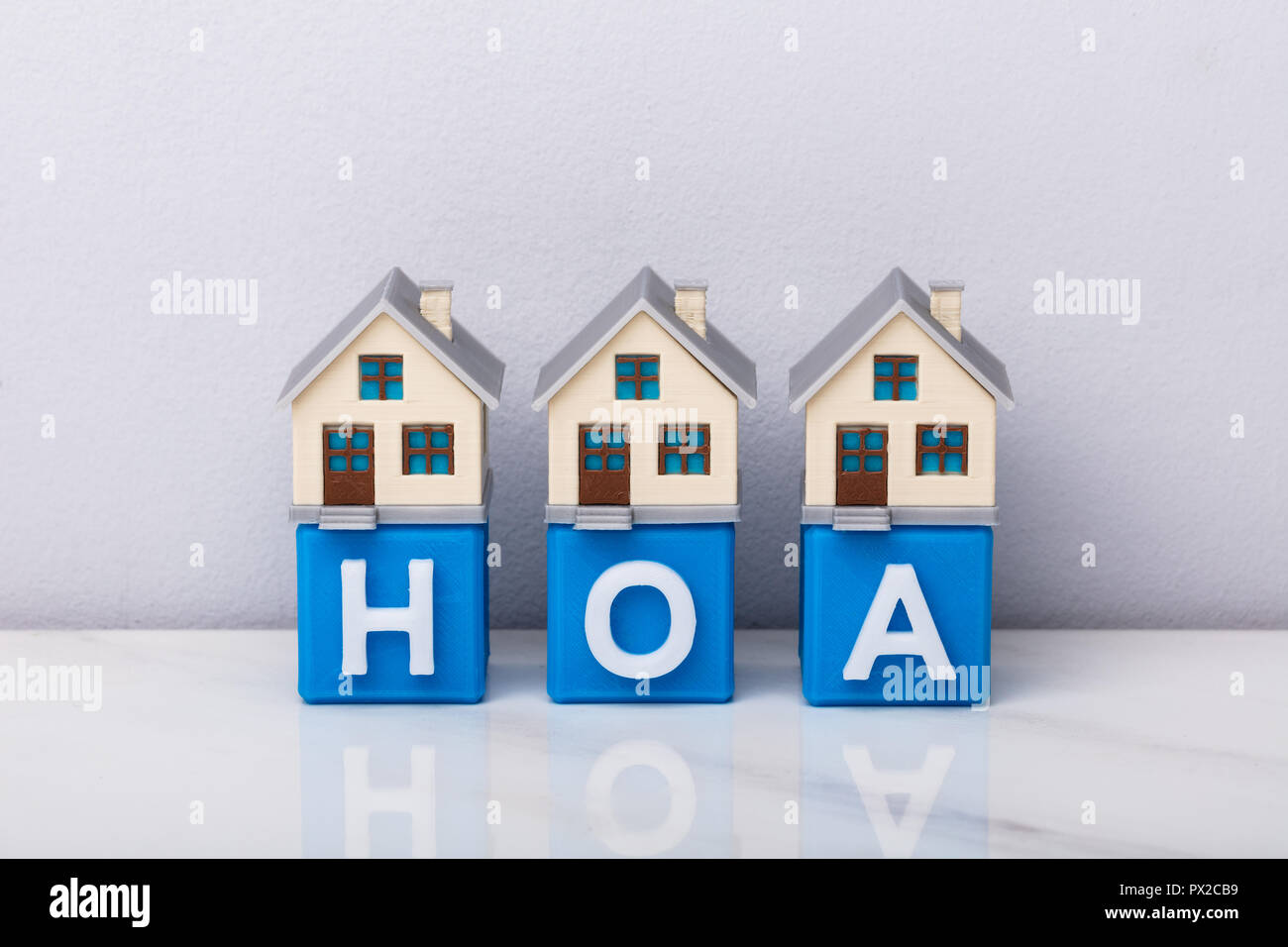 Row Of House Models On Blue HOA Cubic Blocks Over Reflective Desk Stock Photo