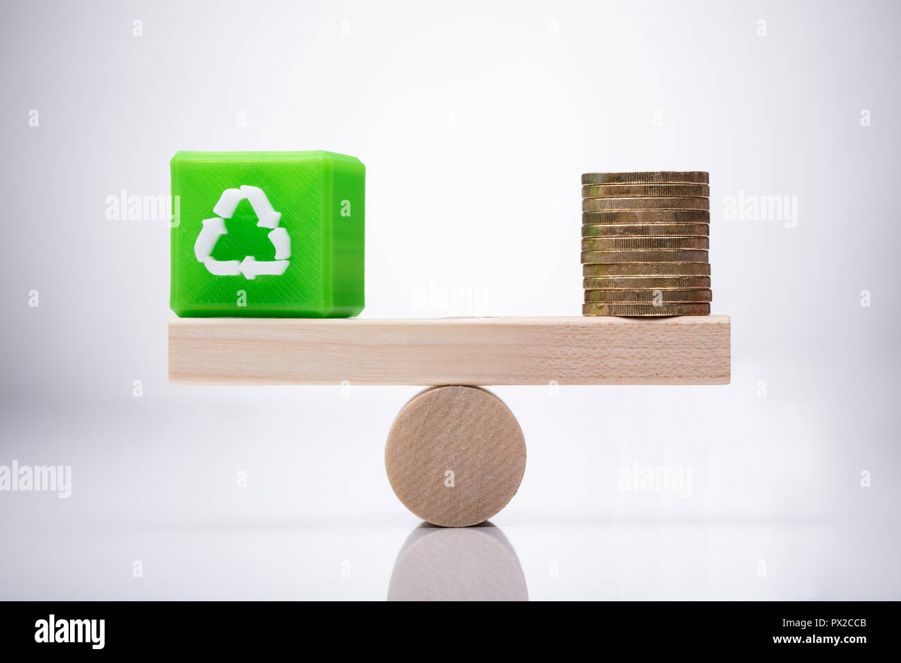 Green Cubic Block With Recycle Symbol And Golden Coins Balancing On Wooden Seesaw Stock Photo