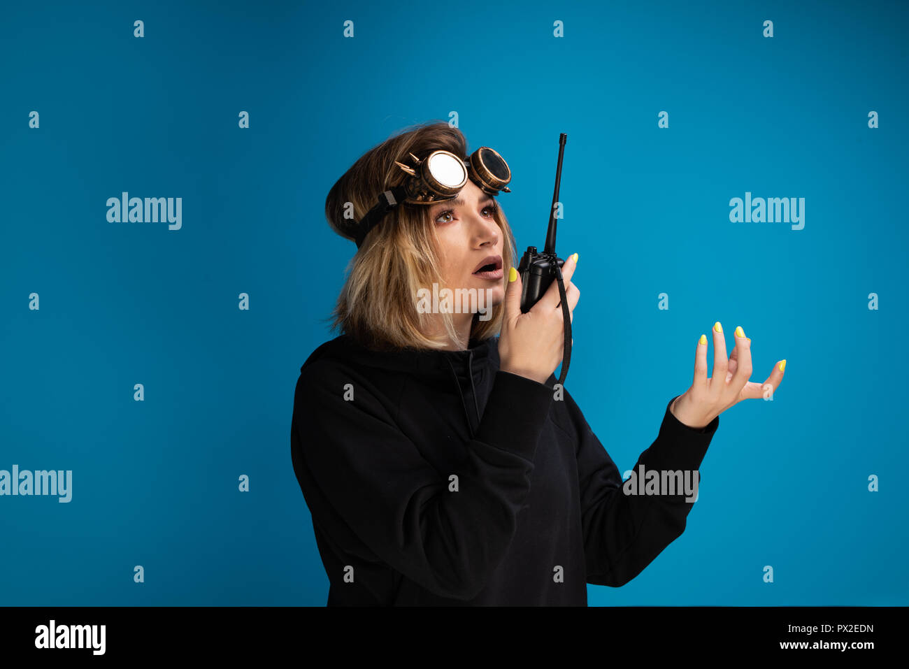 Woman using walkie talkie to communicate while wearing steam punk glasses  on her head. Disapproving expression displayed Stock Photo - Alamy