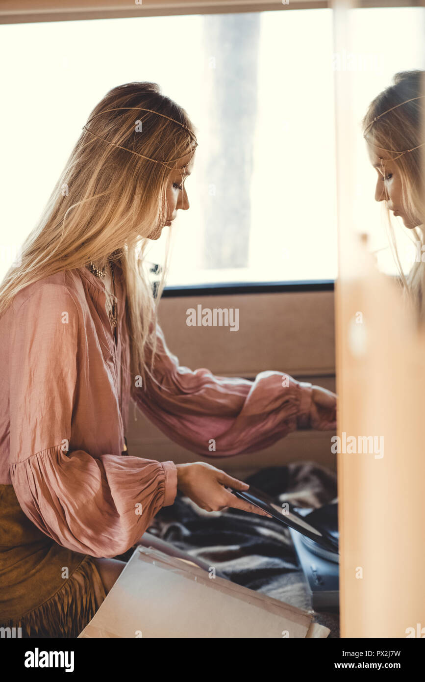 blonde hippie girl putting vinyl record into player inside camper van Stock Photo