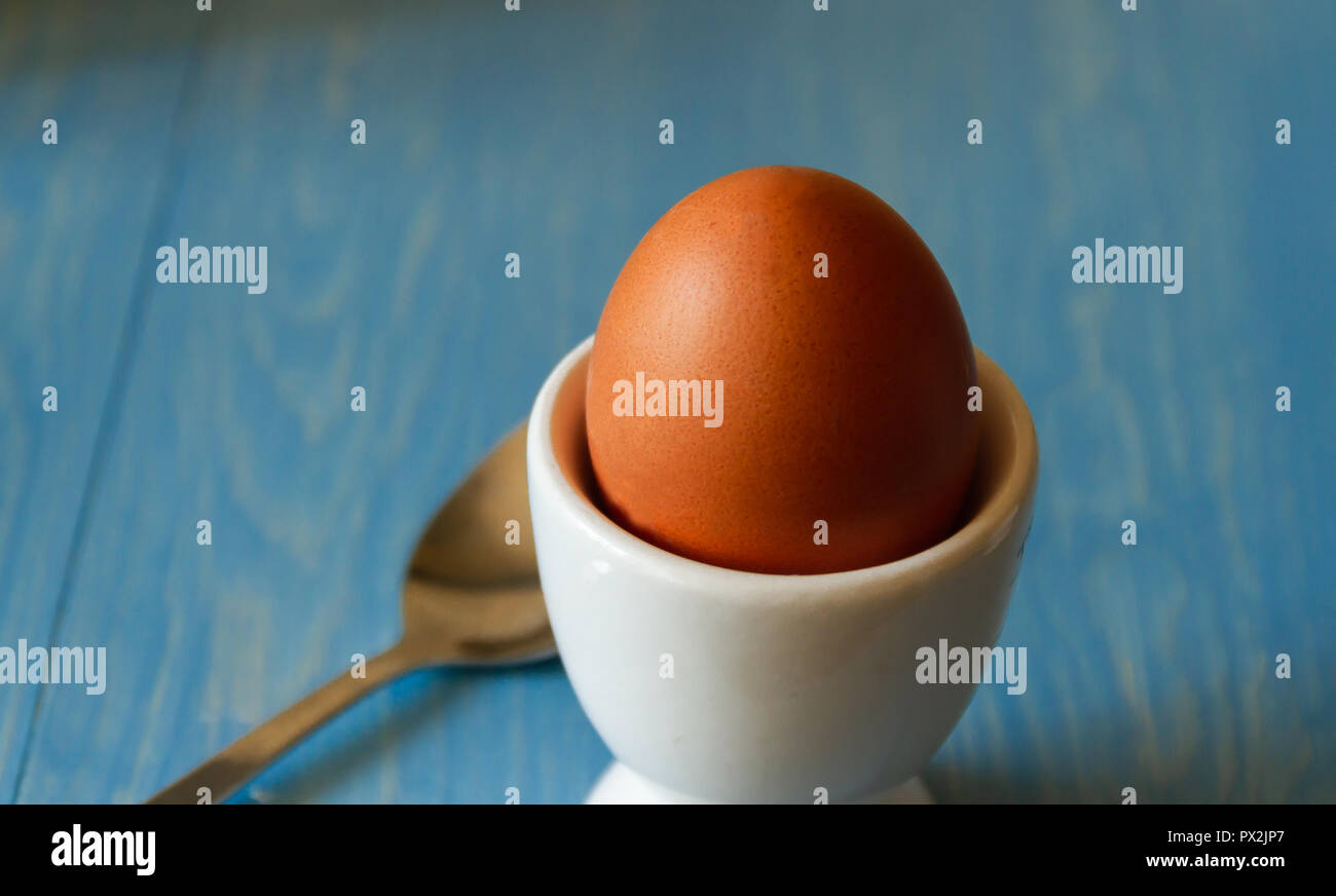 Boiled egg in a white egg cup with spoon on a blue background Stock Photo