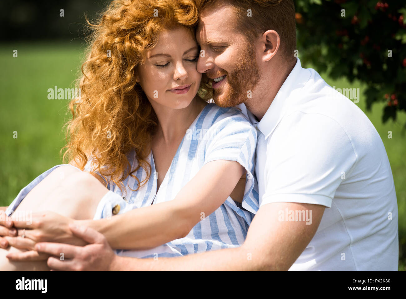 selective focus of smiling redhead couple sitting outdoors Stock Photo