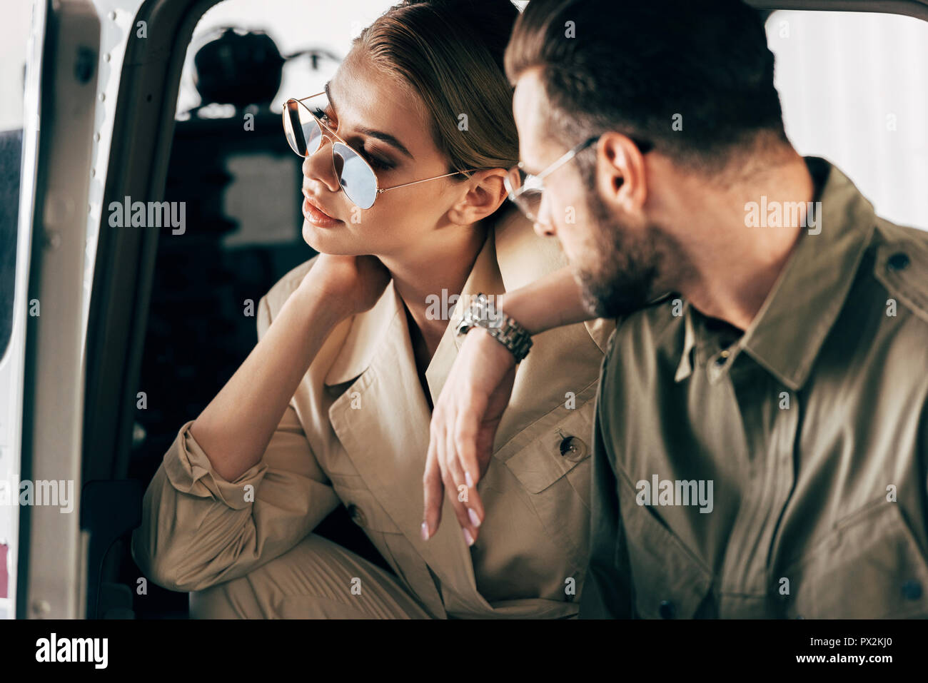 selective focus of attractive woman in sunglasses sitting in airplane while her boyfriend standing near plane Stock Photo