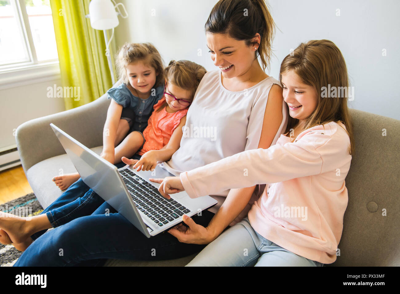 mother and daughters on sofa at home using laptop Stock Photo
