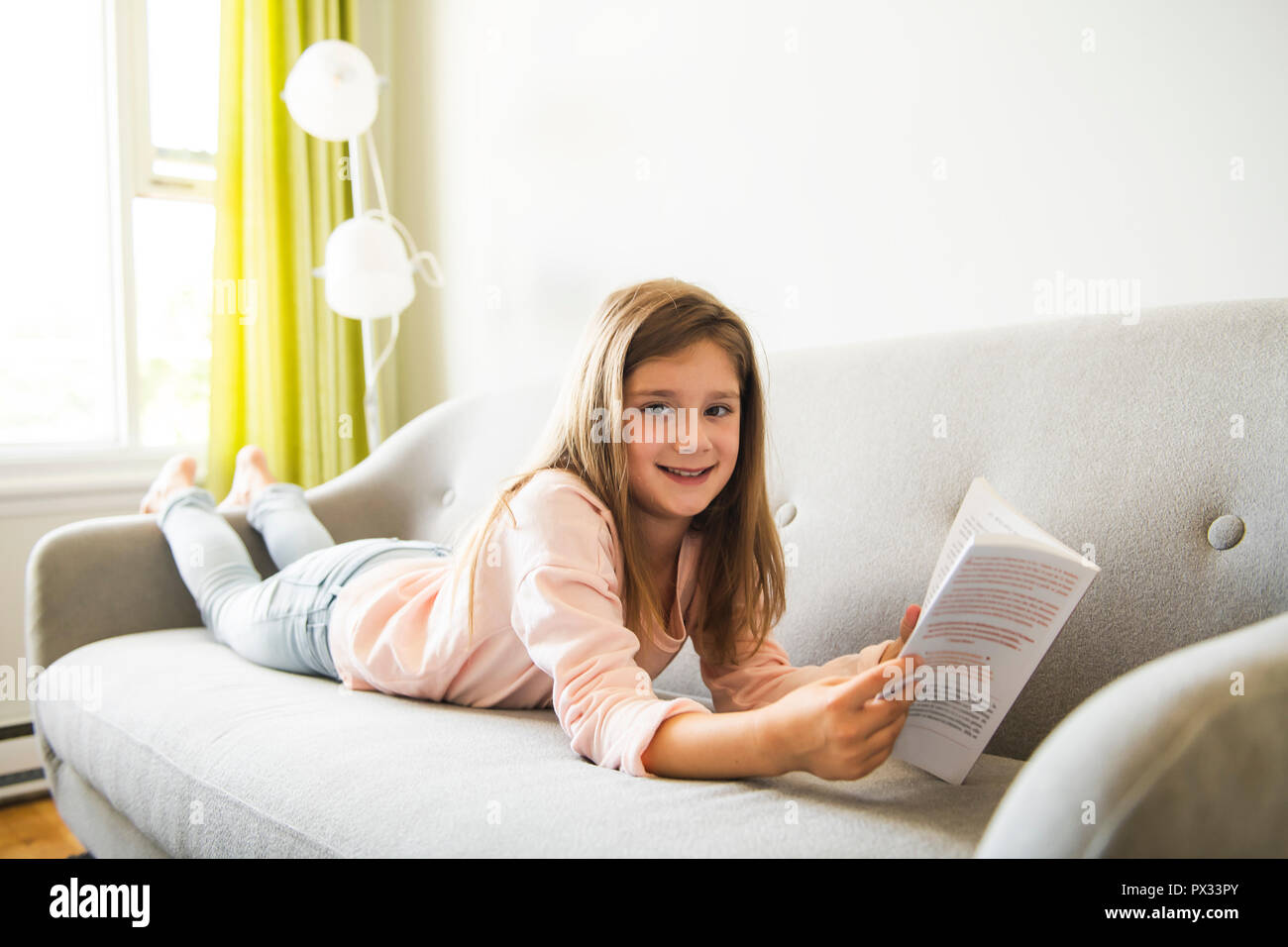 Girl Reading Book On Sofa In Living Room At Home Stock Photo - Alamy