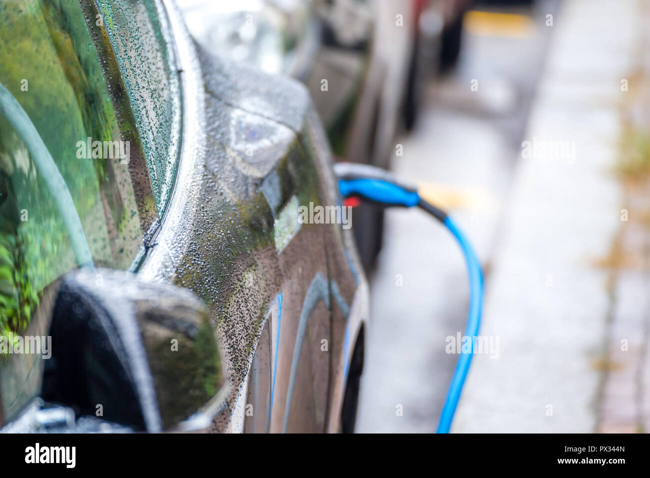 raindrops wetting car while charging plugged into a power station on a street Stock Photo