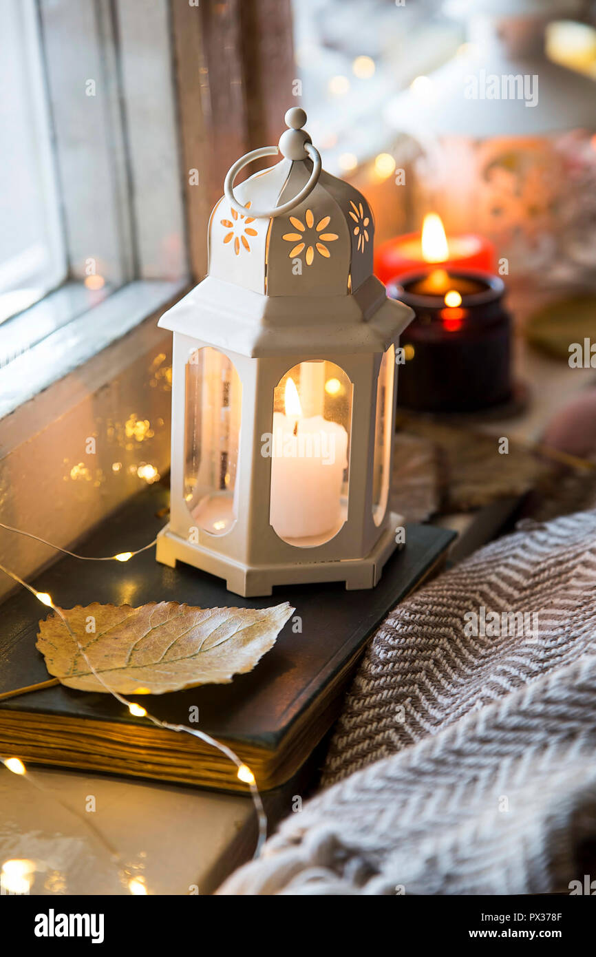 Autumn or winter lifestyle indoor window decorations with candle lantern,  book and blanket, cozy indoor setting Stock Photo - Alamy