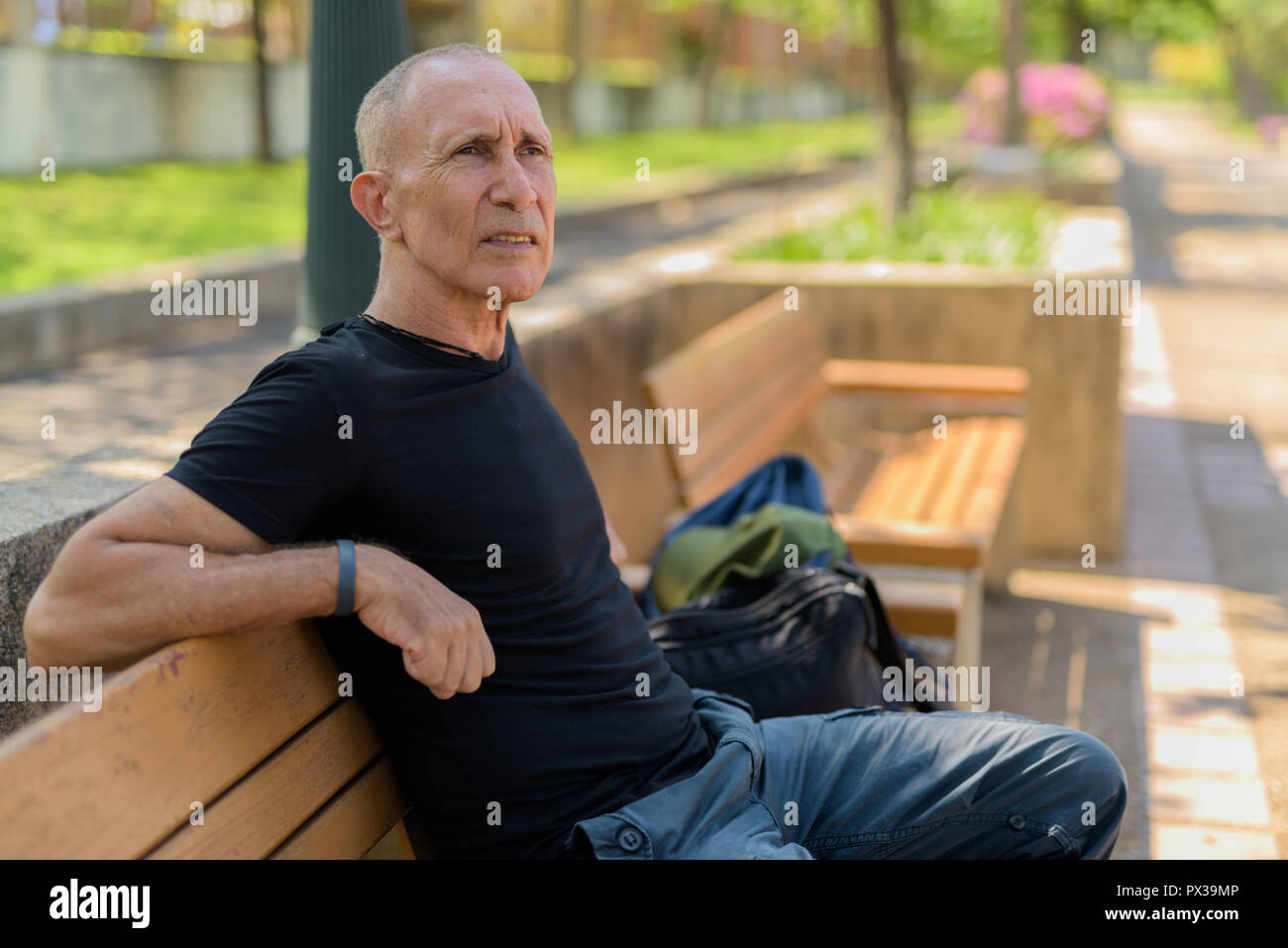 Bald senior tourist man thinking on the wooden bench at peaceful Stock Photo