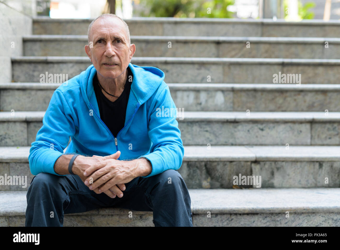 Bald senior man leaning arms on knees while sitting on the stair Stock Photo