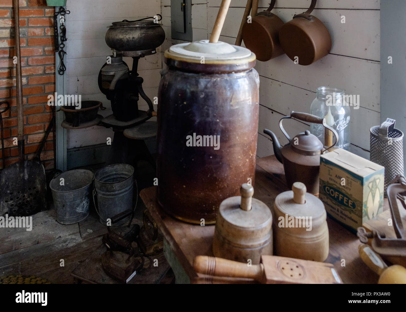 Interior of Vintage Texan Home with antique butter churns and other kitchen items. Brick wall, shovel. Chestnut Square Historic Village, McKinney,Texa Stock Photo