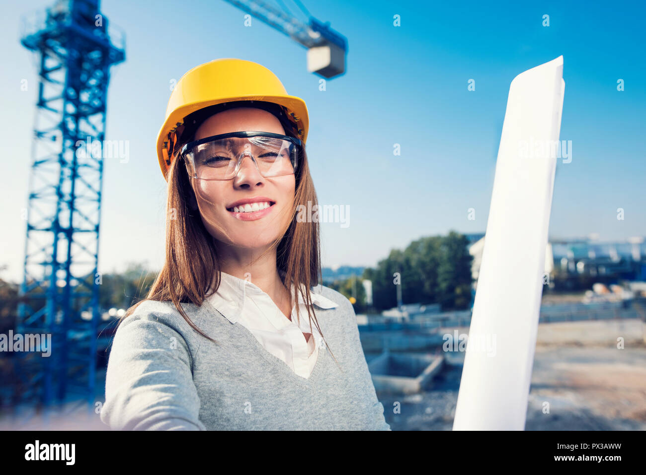 Beautiful woman civil engineer is taking a self portrait in her work in front of a crane Stock Photo