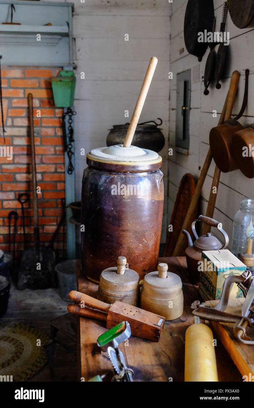 Interior of Vintage Texan Home with antique butter churns and other kitchen items. Brick wall, shovel.Chestnut Square Historic Village, McKinney,Texas Stock Photo