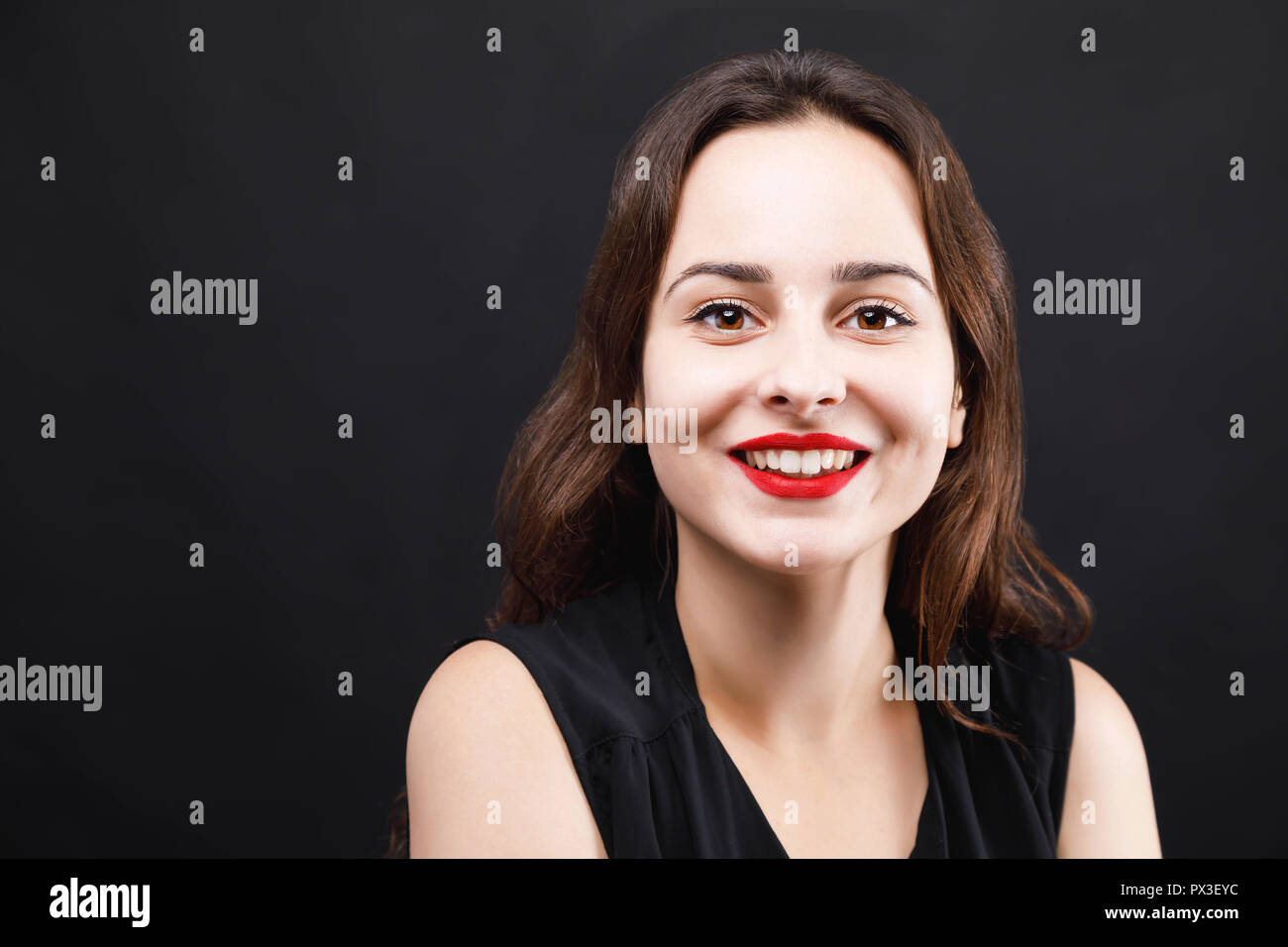 Portrait of cute smiling brunette woman wearing black dress standing on ...
