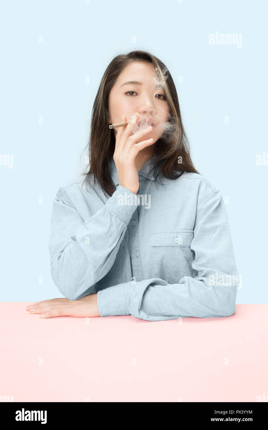 Handsome young korean women smoking cigar while sitting at table at studio. Trendy colors Stock Photo