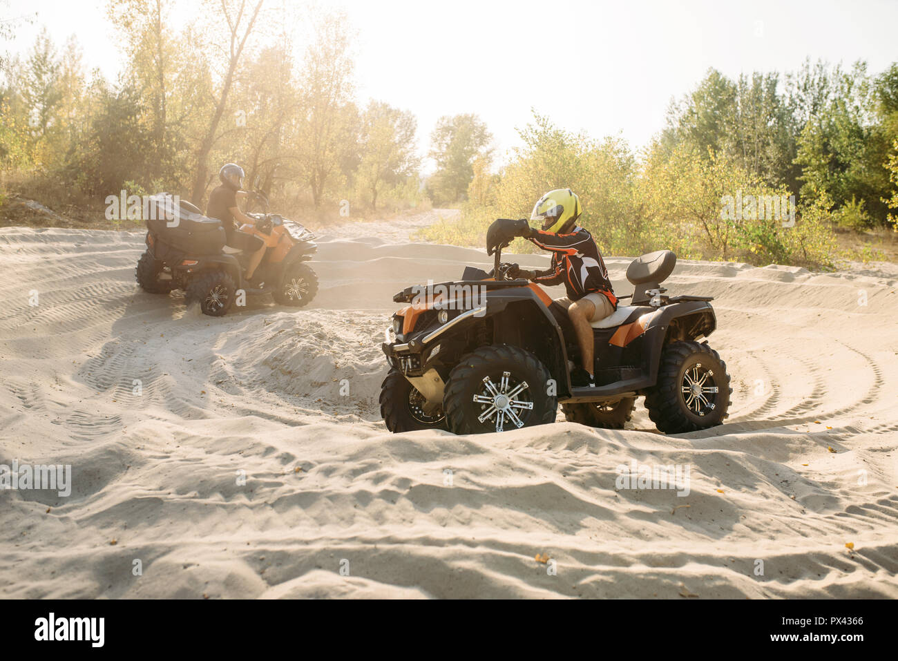 Two atv riders in helmets ride in a circle on sand Stock Photo - Alamy