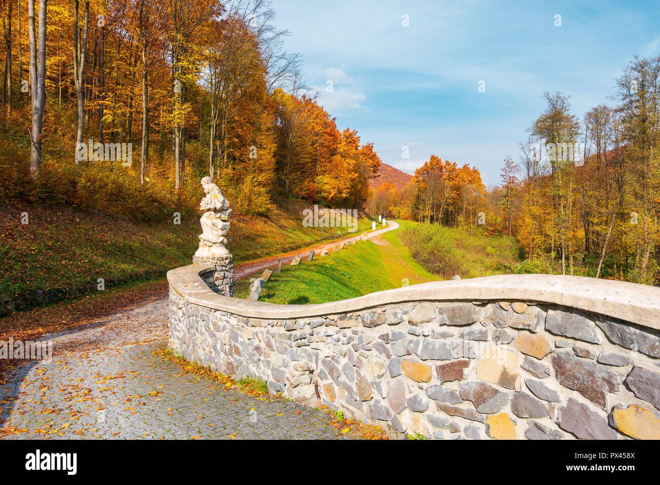 path from the stone bridge in to the forest. trees in fall colors. blue sky above the landscape Stock Photo