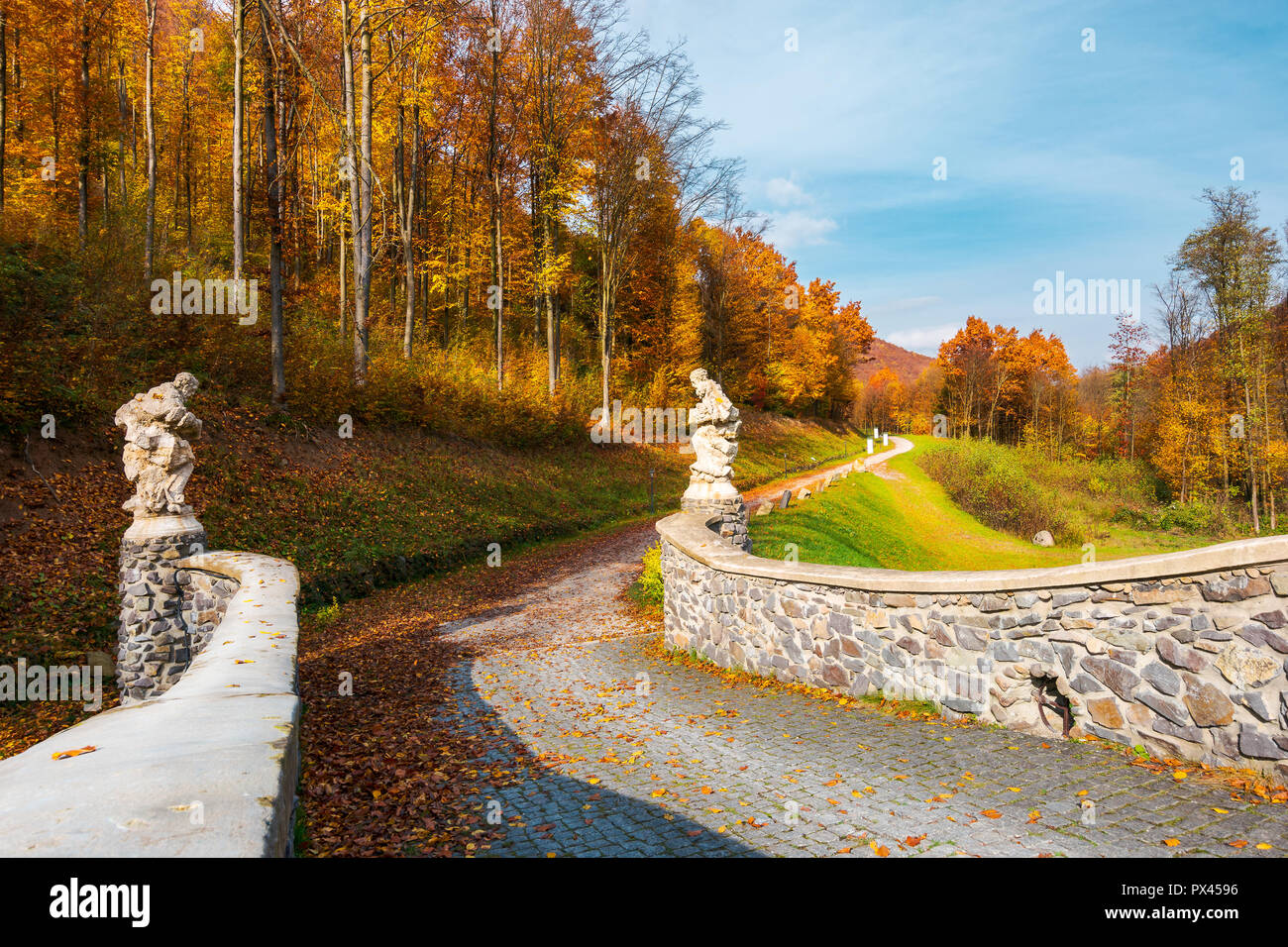 path from the stone bridge in to the forest. trees in fall colors. blue sky above the landscape Stock Photo