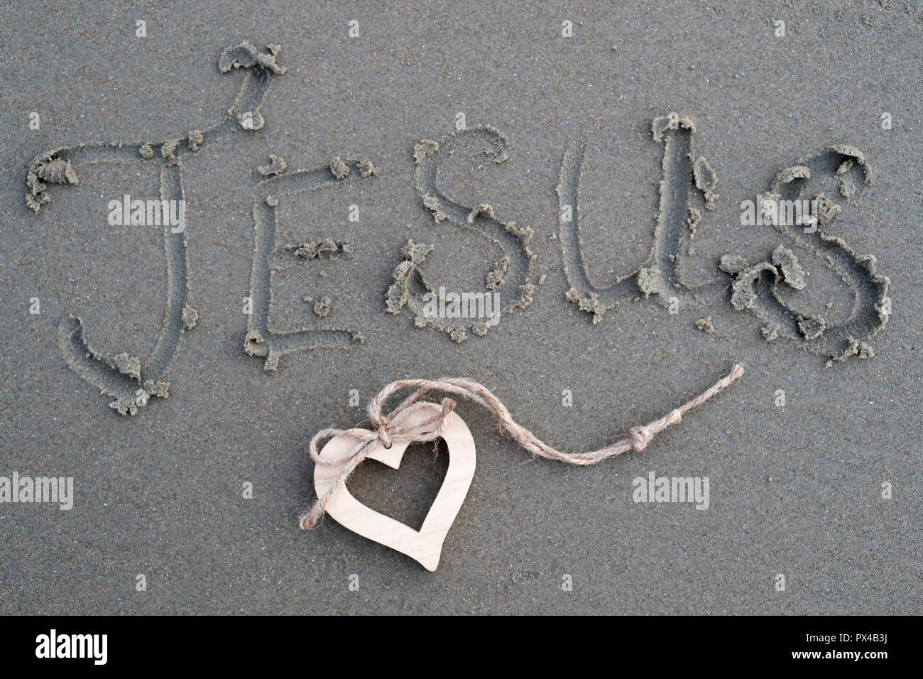 A wooden heart and  the name of Jesus written in the sand. Stock Photo