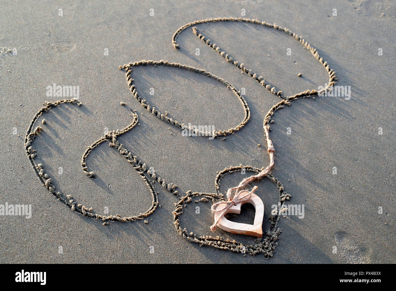 A wooden heart and  the name of God written in the sand. Stock Photo