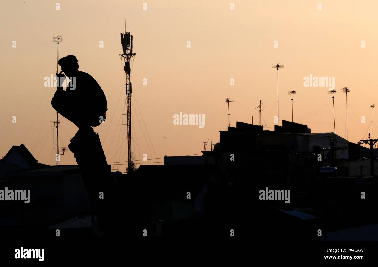 Silhouette of young man against sunset sky and roof house.  Cai Be. Vietnam. Stock Photo
