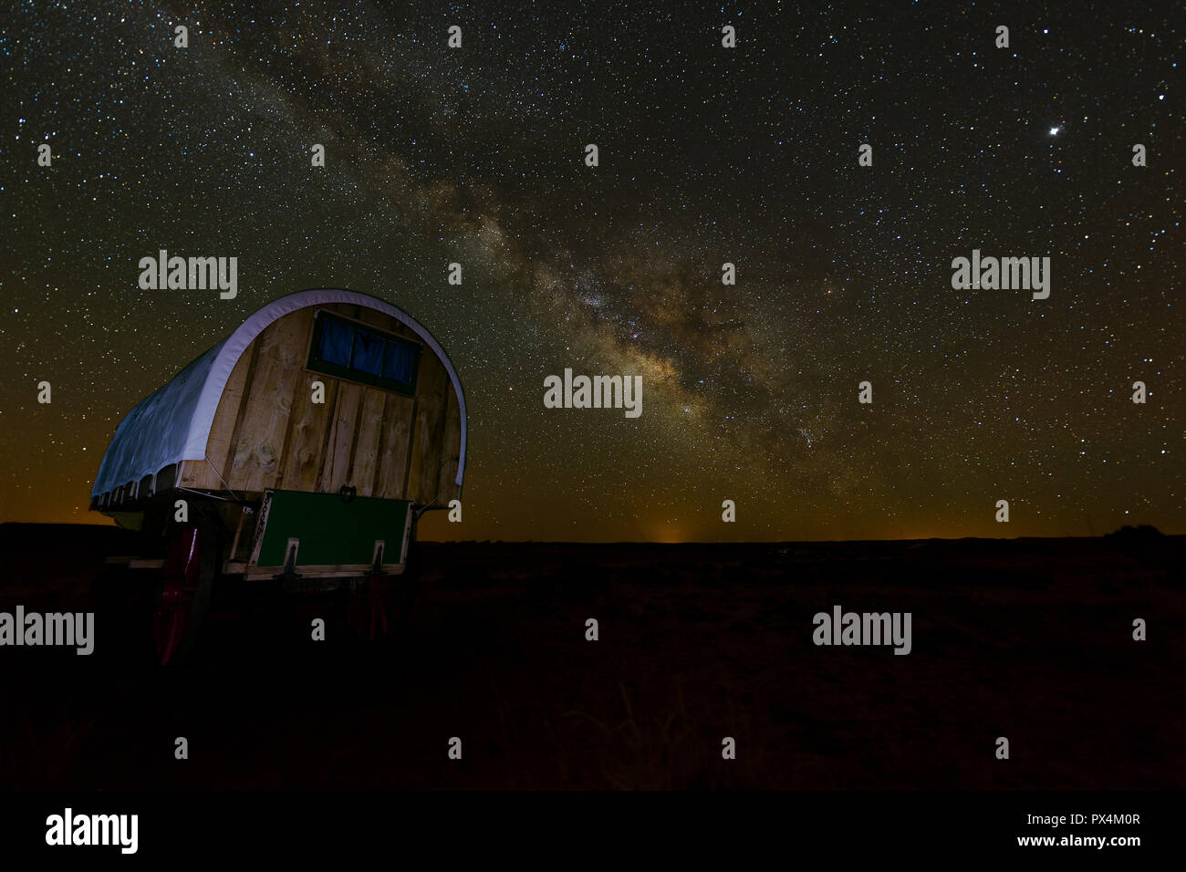 Arizona, USA. A settler-style wagon with red wheels sits underneath a brilliant display of the Milky Way. Stock Photo