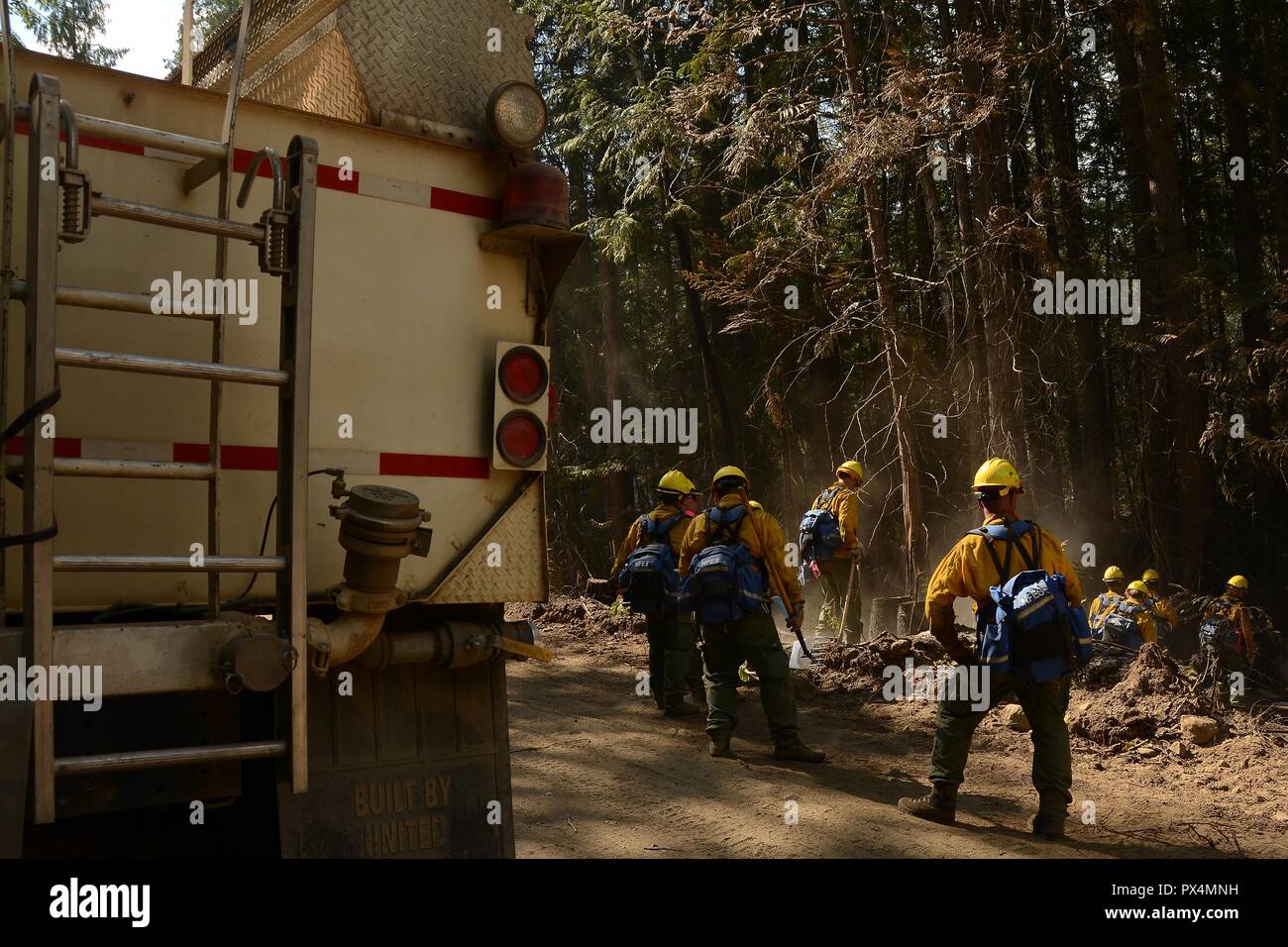 Airmen from the Washington Air National Guard's 141st Air Refueling Wing use rakes and hoses to search for remaining embers in a forested area while fighting the Sheep Creek Fire, with the rear of an emergency support vehicle visible in the left foreground, located in the Sheep Creek area near Northport, Washington, USA, image courtesy Technical sergeant Timothy Chacon and the Joint Forces Headquarters, Washington National Guard, August 6, 2018. () Stock Photo