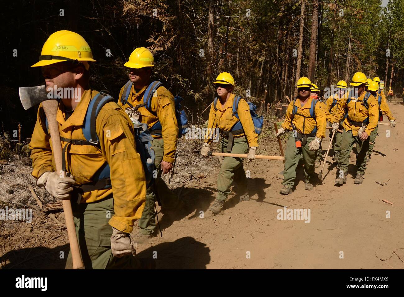 A group of Airmen from the Washington Air National Guard, wearing yellow safety gear and blue backpacks, walk in a line along a dirt road, with forest visible in the background, on their return from fighting the Sheep Creek Fire, located in the Sheep Creek area near Northport, Washington, USA, image courtesy Technical sergeant Timothy Chacon and the Joint Forces Headquarters, Washington National Guard, August 6, 2018. () Stock Photo
