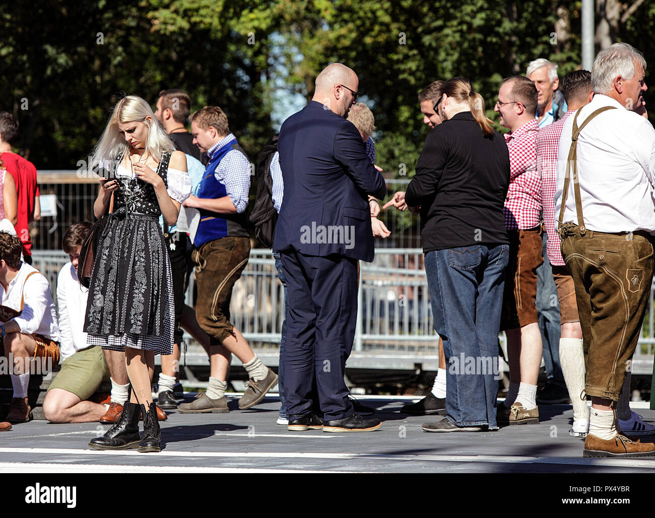 Oktoberfest party goers waiting for the train at Riem Station on the U-Bahn in Munich. Blond German woman holding a mobile phone. Stock Photo