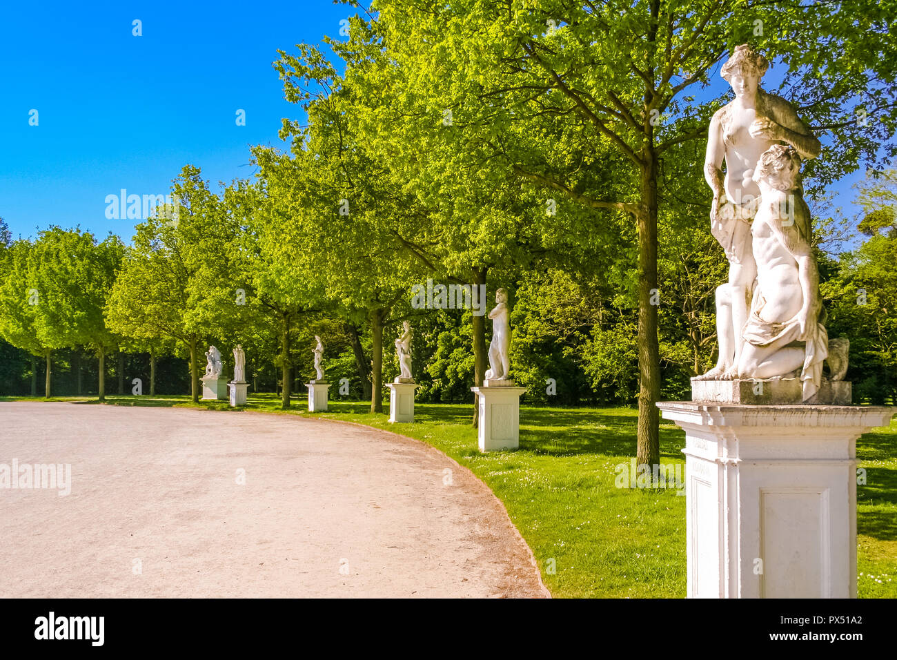Six white baroque sculptures of men and women on pedestals at a curved road in the Karlsaue park in Kassel, Germany on a sunny spring day with nice... Stock Photo