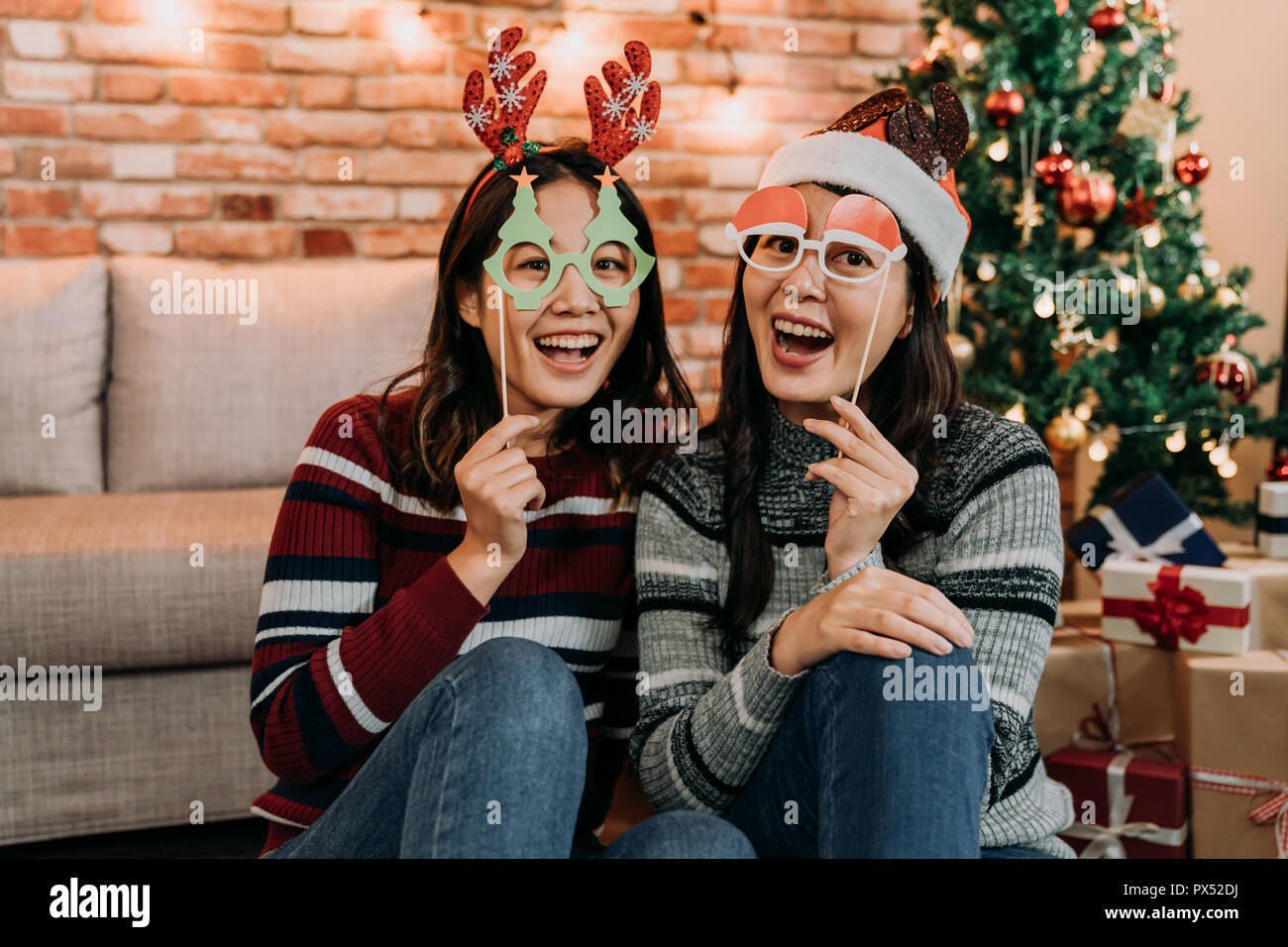 Picture showing two of friends celebrating Christmas at home. young females having fun with fake glasses on face. girlfriends face to camera joyfully  Stock Photo