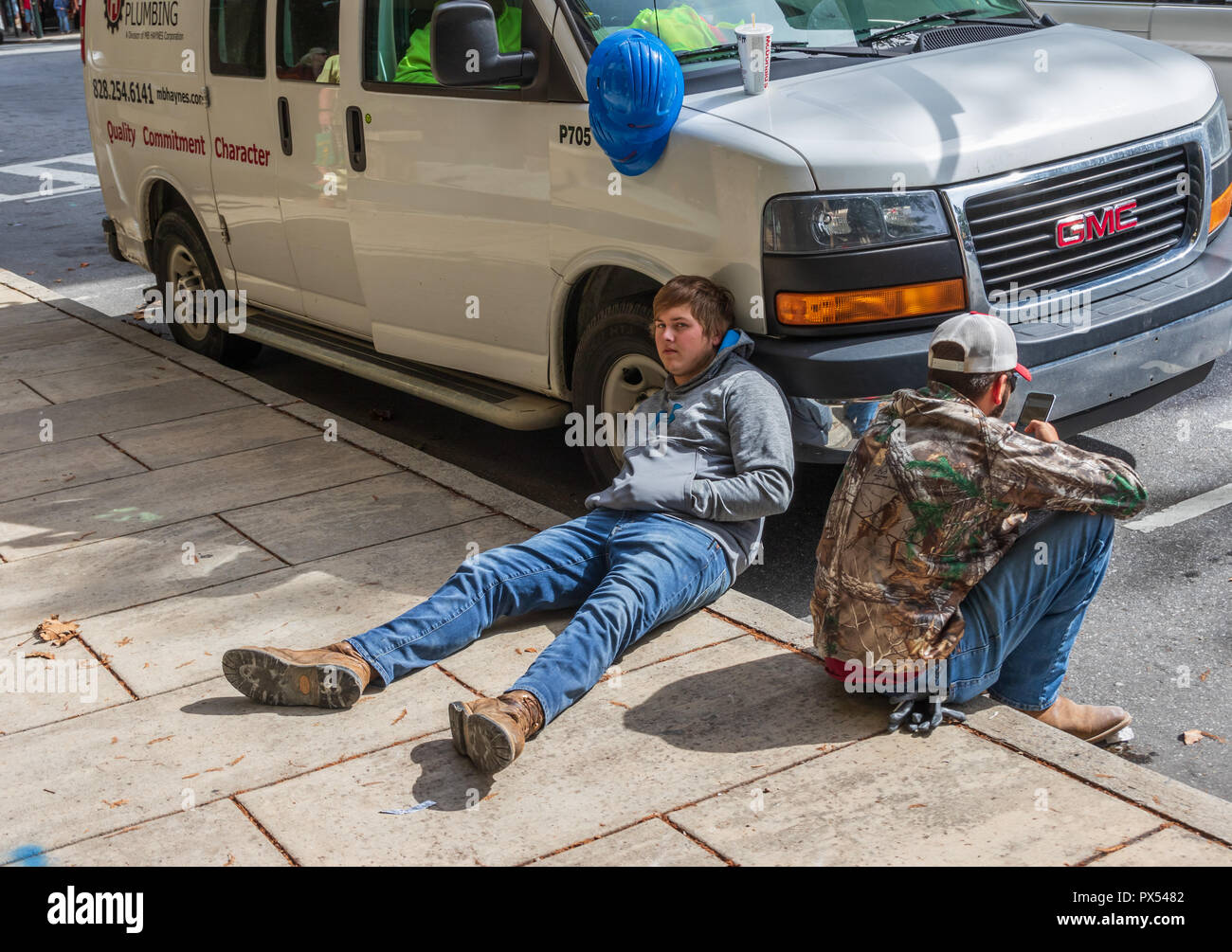 ASHEVILLE, NC, USA-10/17/18: Two young male plumbers taking a break on the sidewalk. Stock Photo